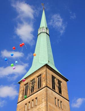 Kirchturm an dem bunte Ballons vorbeifliegen